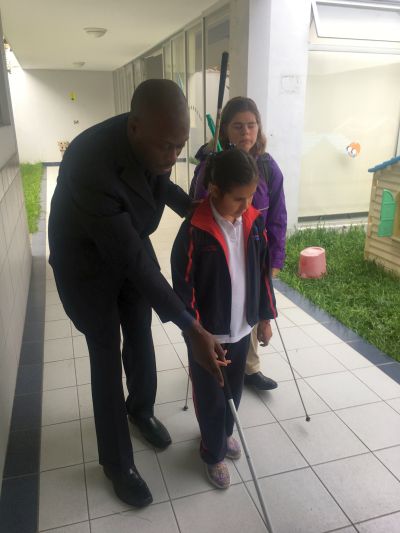 Garrick, a METAS member showing a student how to use a cane while a teacher looks on